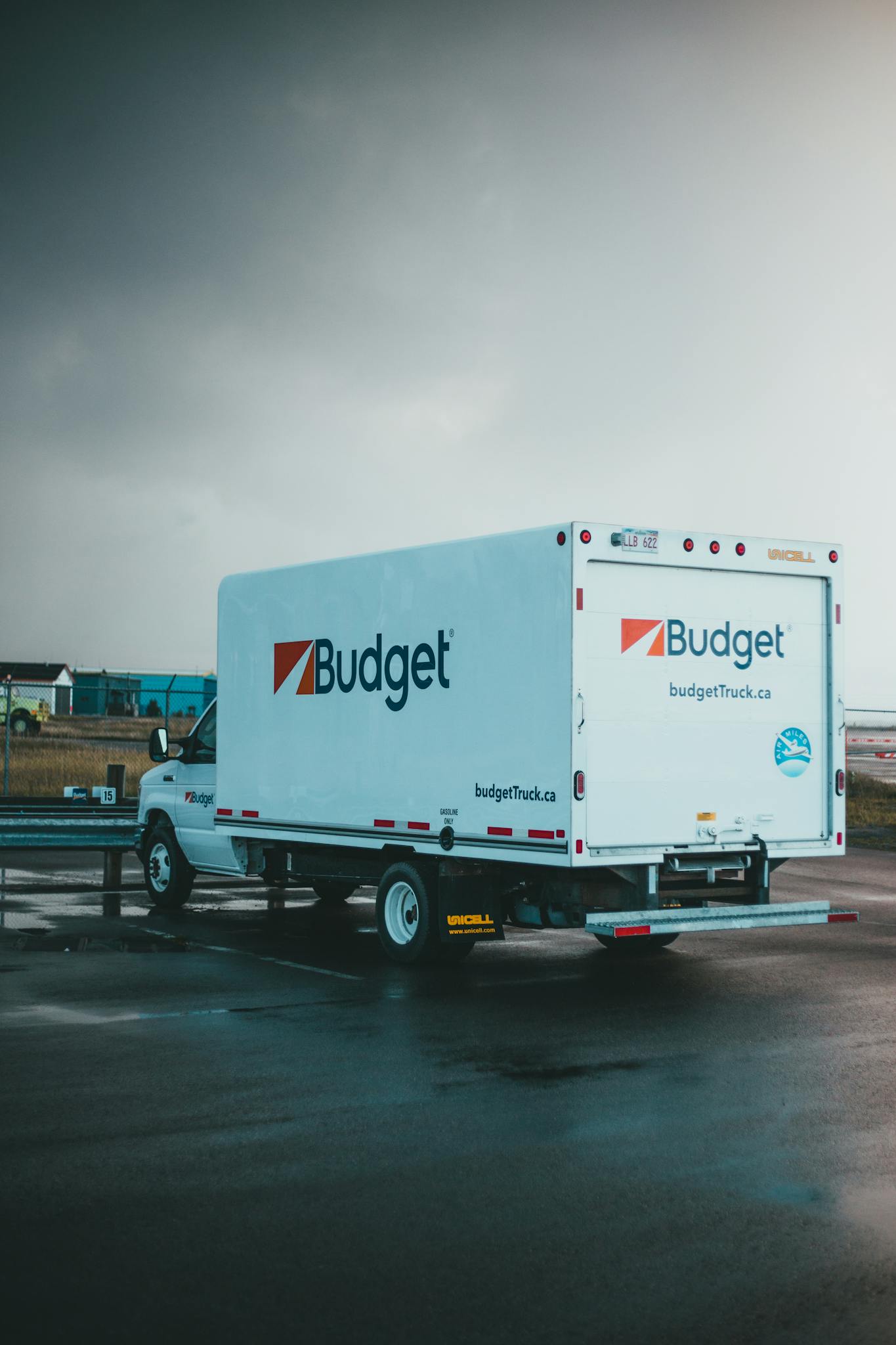 A Budget rental truck parked on a wet asphalt in an outdoor lot under a cloudy sky.