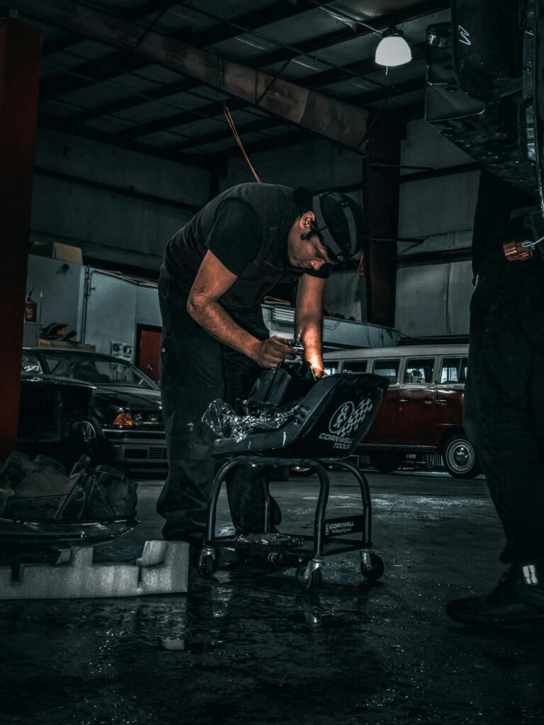 A mechanic focused on a car part repair in a dimly lit auto body shop.